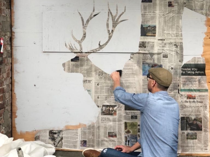 Artist Ray Monde wheatpasting a paper cut out of an elk
