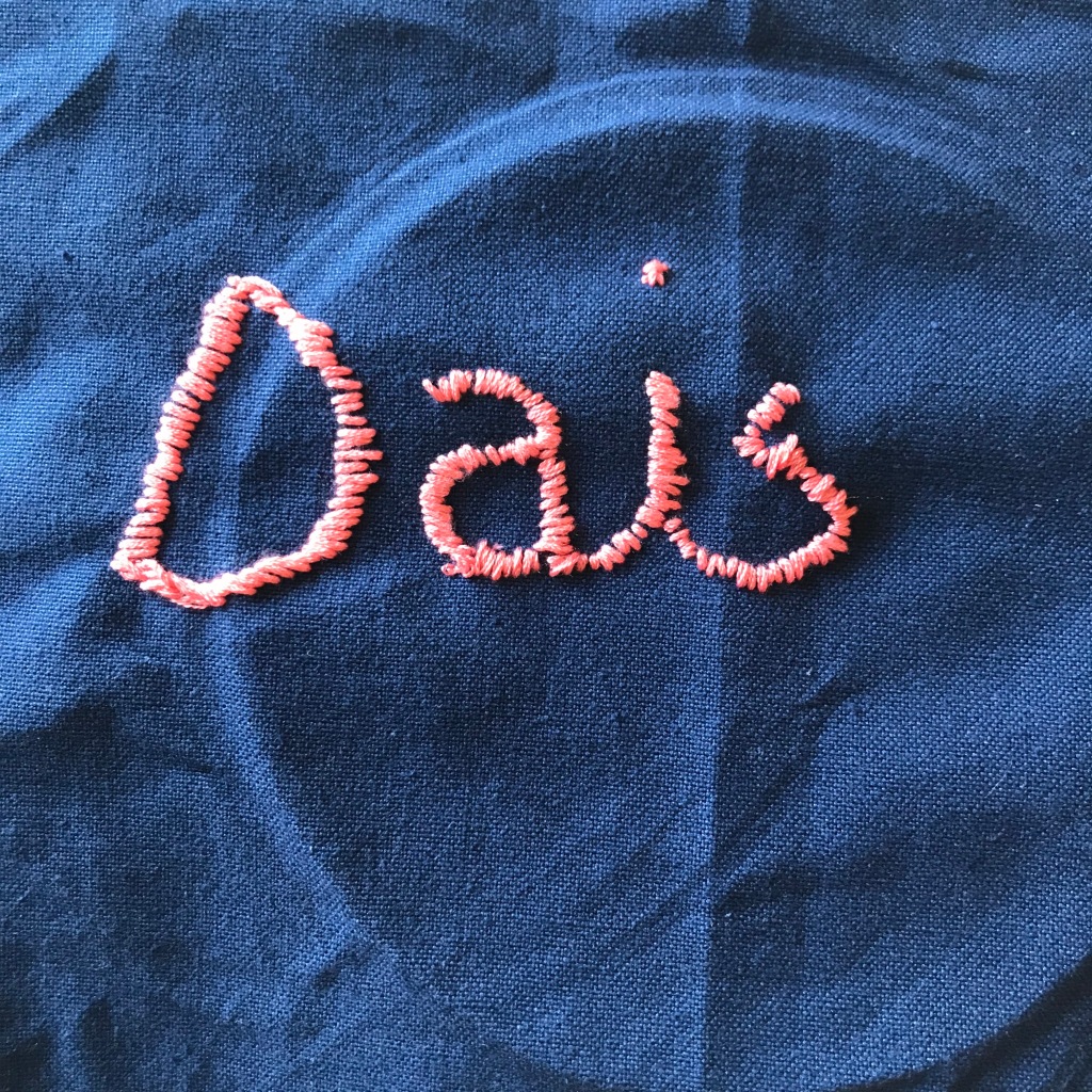 A blue piece of cloth with pink stitching which reads Dais